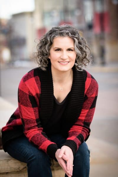 Carla Laureano sitting on a stone wall on a small town main street